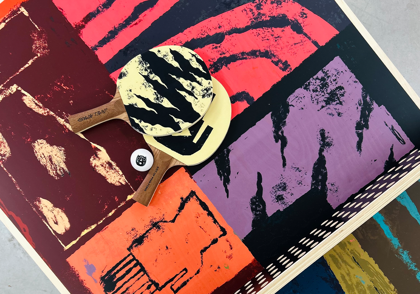 Jamel Armand ping pong table with paddles and ball photographed from above.