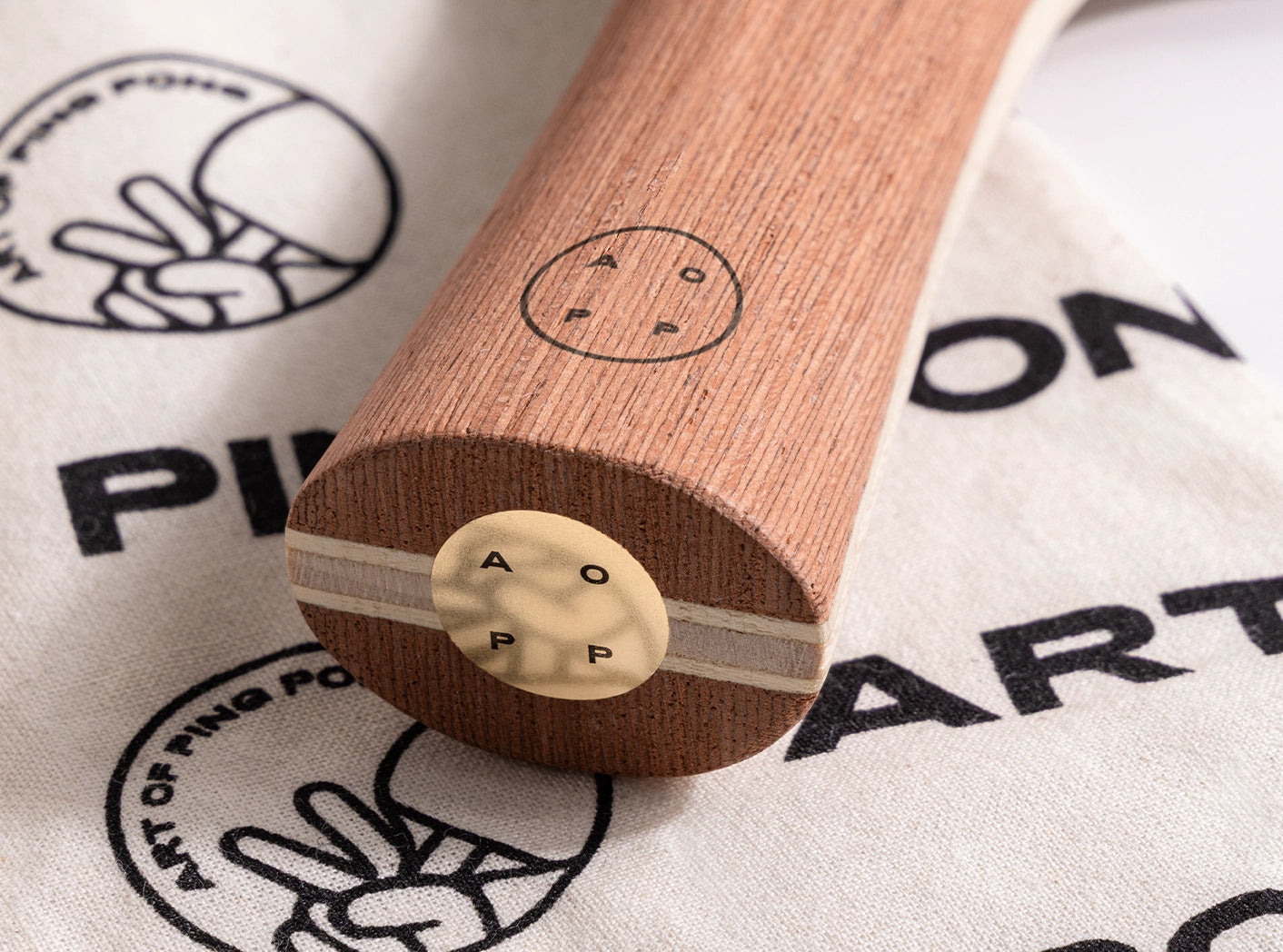 Table tennis paddle with black rubber and wooden handle and a brass disc in base on a branded 'Art of Ping Pong' bag