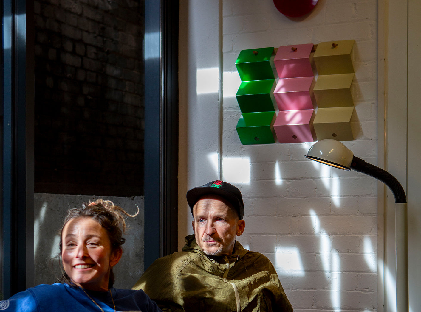 The founders of Art of Ping Pong sitting beneath their Faces ArtNet mounted on a wall