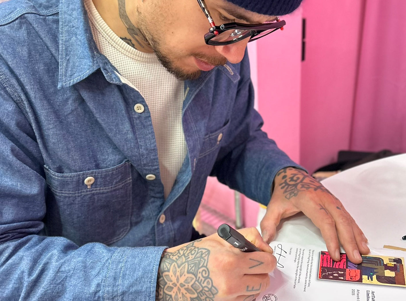 Jamel Armand with tattoos and glasses signing Authenticity Certificates with a pen.