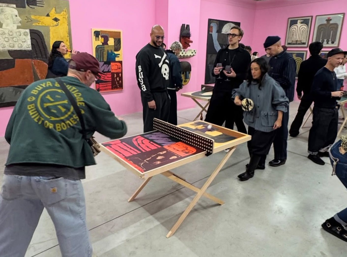 Group of people in a gallery setting with art on the walls and a ping pong table.