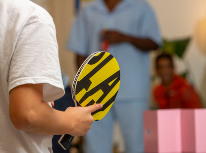 Person holding a yellow and black paddle with 'Play Nice' branding, blurred background