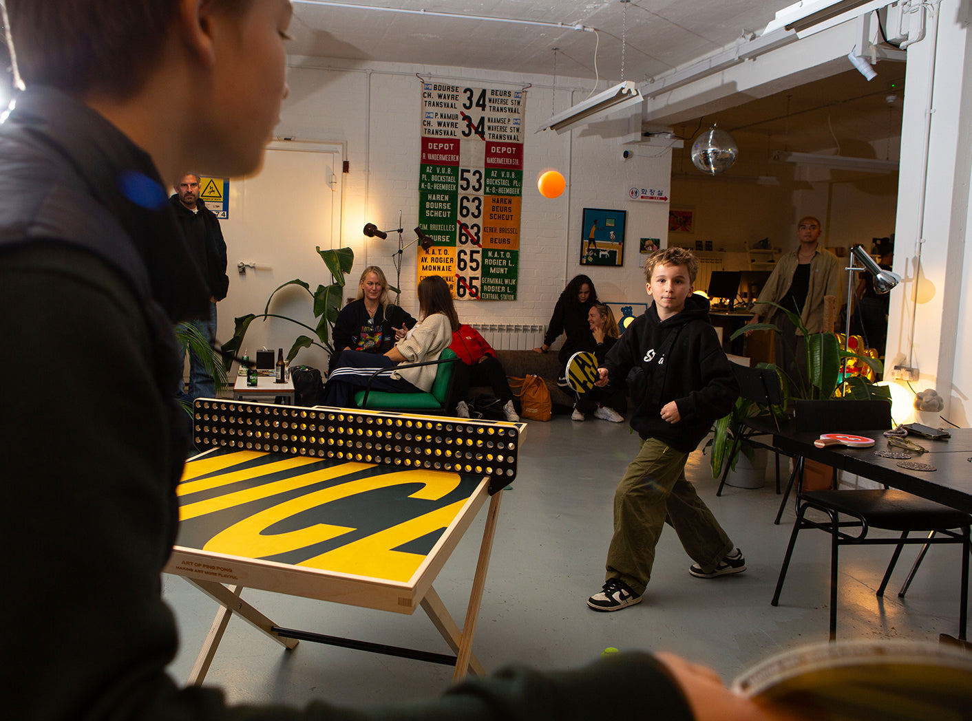 Person playing ping pong in a casual indoor setting with sports memorabilia on the wall.