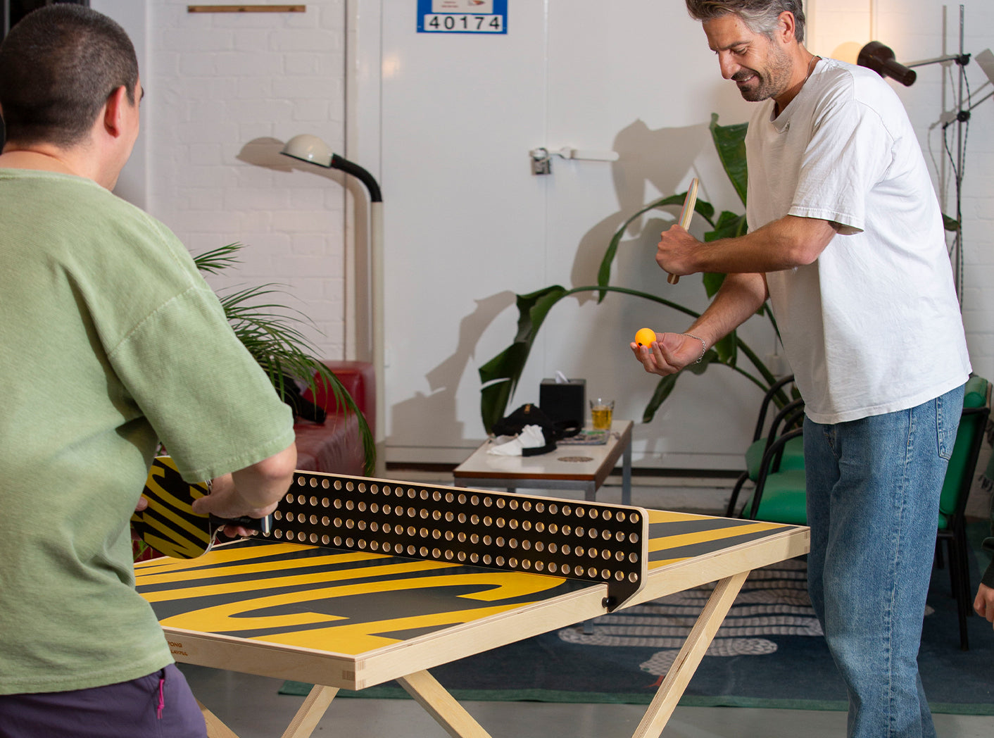 Two men playing table tennis on an Art of Ping Pong ArtTable in a casual indoor setting.