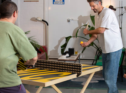 Two men playing table tennis on an Art of Ping Pong ArtTable in a casual indoor setting.